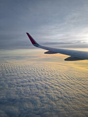 Peaceful aerial view from airplane window to the large wing soaring over a sea of clouds with the sun rising above the horizon, casting a warm glow and illuminating the cloudscape during flight