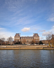Beautiful view of the Hotel de Ville from the Seine riverside, showing the grand Neo-Renaissance facade and the riverbanks lined with trees and stone embankments