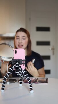 Vertical screen beauty blogger records makeup content with smartphone on tripod demonstrating cosmetics setup at home studio creating social media tutorial lifestyle scene