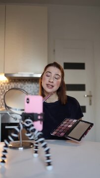Vertical screen beauty blogger reacts with open mouth while demonstrating blush technique filming casual makeup talk at home holding palette and brush lifestyle vibe tody