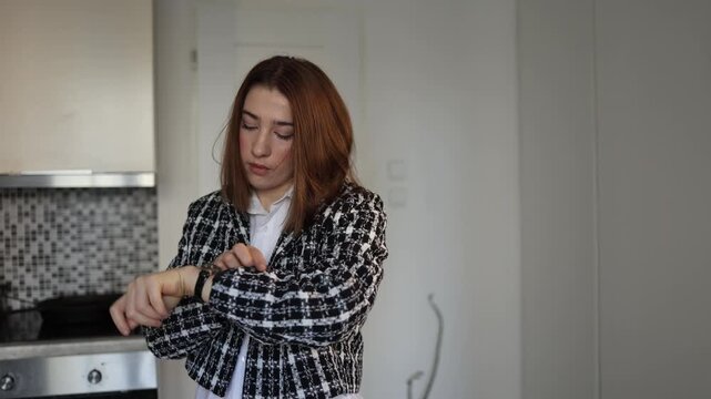 Young woman calmly checks the time on her watch while getting ready at home preparing to leave for the day with a focused expression in a quiet morning moment inside her apartment
