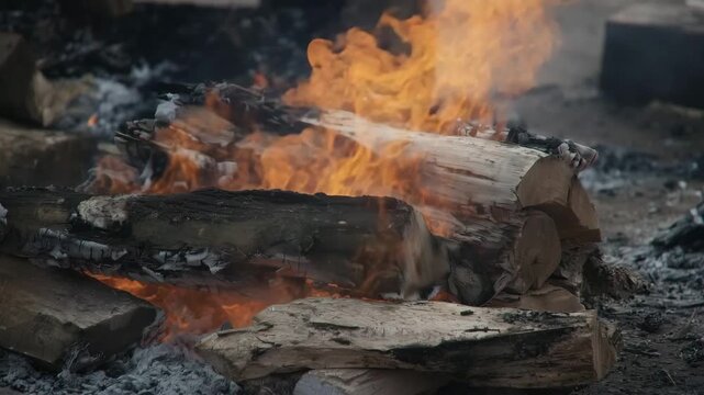 a funeral pyre fire burning intensely, stacked wooden logs with bright orange flames, ash and charcoal embers surrounding the woo 