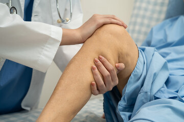 Doctor checking Asian elderly woman patient with scar knee replacement surgery in hospital.