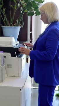 Businesswoman in a blue suit operates a multifunction printer in an office, making copies of important documents while maintaining a focused and professional demeanor