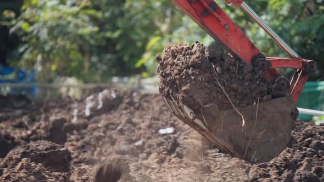 Backhoe excavator working in soil preparation area for construction foundation, clearing and leveling ground on rural job site.