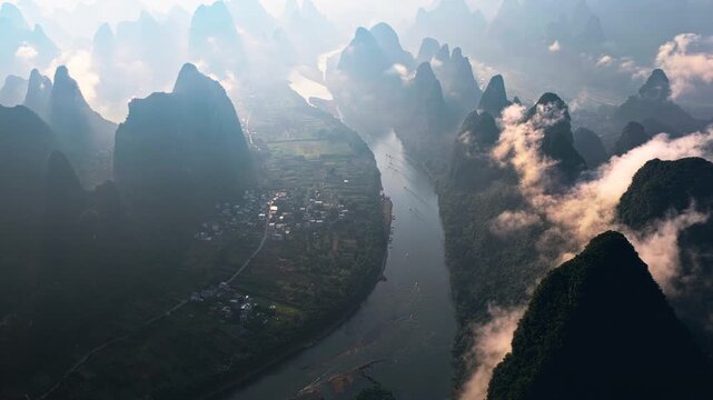 Aerial shot of the Li River winding through karst mountains and a small village in Guilin, China during a misty sunrise.