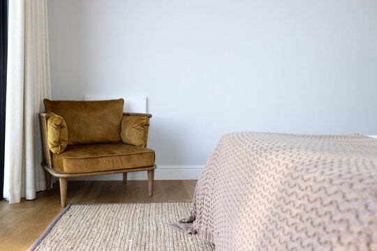 Mustard velvet armchair is anchoring minimal bedroom corner near bed with knit blanket