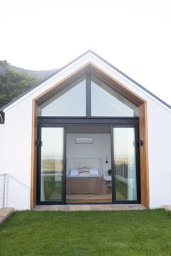 Modern gabled building showing black-framed sliding doors with tufted headboard and coastal horizon