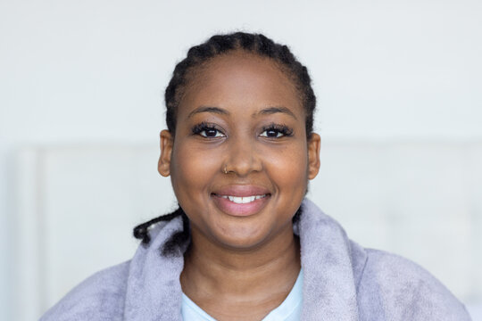 African American woman smiling while wearing blue top with lavender robe and nose ring in bedroom