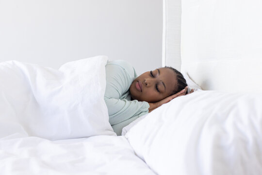 African American woman lying on side on bed with white duvet pillow wearing mint long-sleeve top