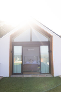 Small studio facade featuring wood frame sliding glass doors opening onto lawn, bed, striped pillow