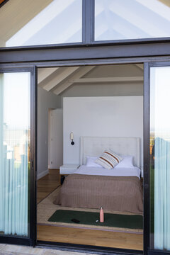 Tufted bed is sitting centered near sliding glass doors with sheer curtains and daylight