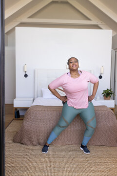 Mid adult African American woman exercising at foot of bed in bedroom with teal leggings headset