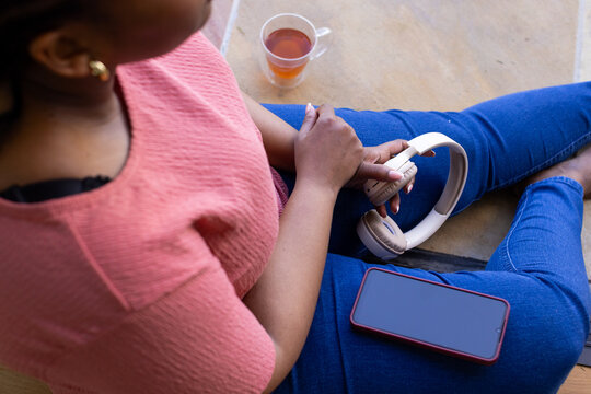 White over-ear headphones are resting on tiled floor near red-case smartphone and tea cup