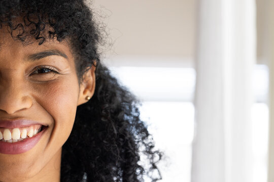 African American woman smiling and facing camera by bright window showing blinds, gold stud earring