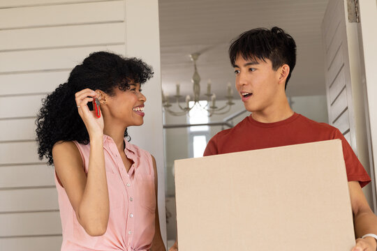 Diverse couple smiling, woman holding red key fob, pink sleeveless shirt, man carrying box in foyer