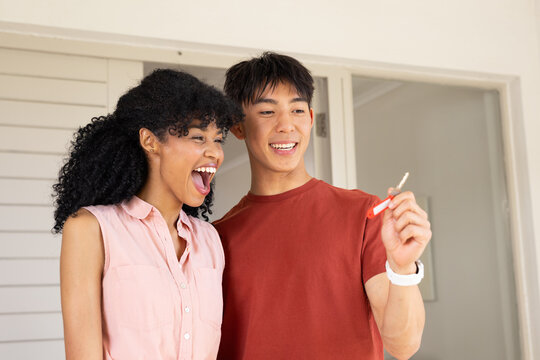 Diverse couple standing at house entrance holding metal key with red fob and wearing white watch