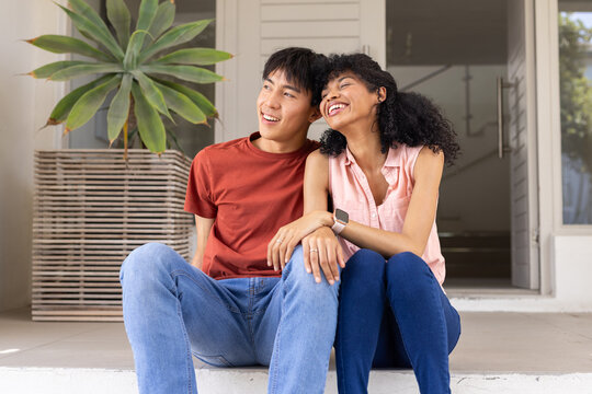 Diverse couple sitting on stoop leaning, woman wearing smartwatch, ring visible, succulent nearby