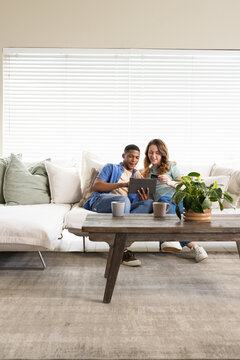 Couple sitting on sectional sofa using tablet while woman holding payment card near coffee table