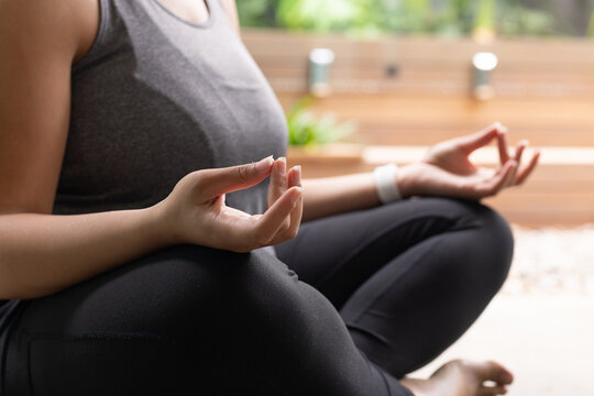 Hands are forming meditation mudra on yoga mat with white watch and blurred plants