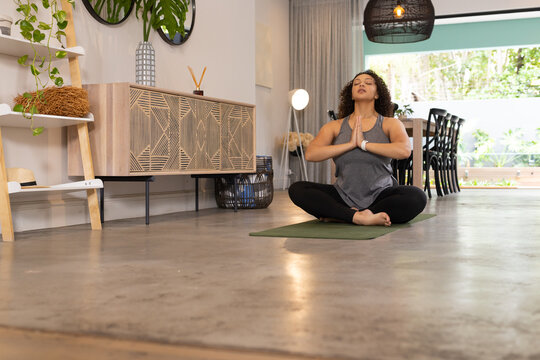 African American woman doing yoga on green mat in living-dining wearing grey tank and fitness watch