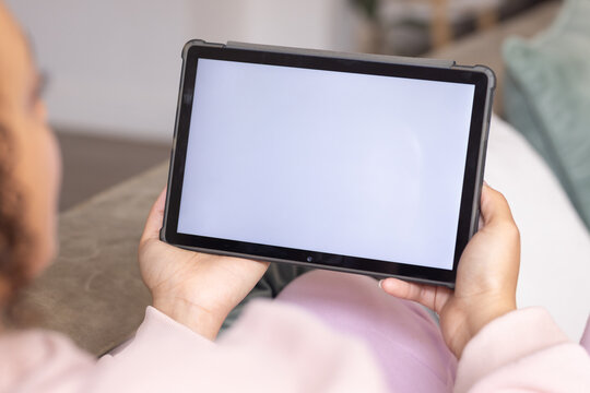 Tablet is being held horizontally on sofa at chest level, screen bright white in protective case