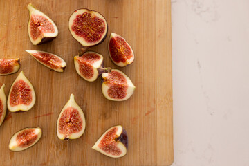 Halved and quartered figs are resting on wooden board by white stone countertop with juice stains