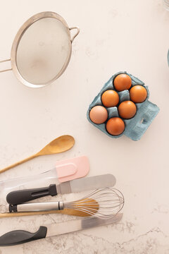 Blue pulp egg carton is resting on pale marble worktop with utensils overlapping left, copy space