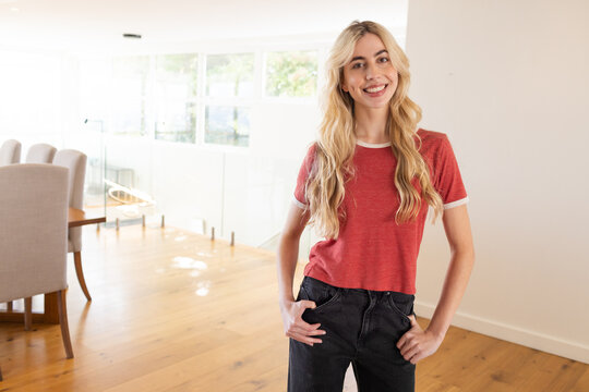 Woman standing smiling on right in modern home in red T-shirt dining table, copy space