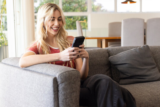 Woman sitting on gray sofa in living area wearing red short-sleeve tee holding phone and smiling