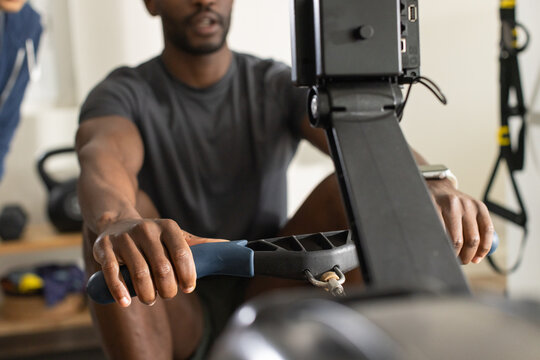 Diverse men rowing, gripping rower handle at gym, wearing dark gray shirt and smartwatch