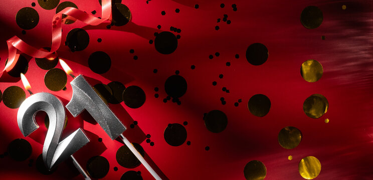 Concept of celebrating birthday and anniversary. Number 21 twenty-one silver celebration birthday candle on festive red background with large golden confetti. Twenty-one years birthday. - Powered by Adobe