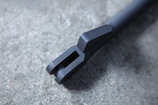 An extreme close-up of a textured, matte black mechanical component, likely a clevis or mounting bracket, resting on a gray concrete surface.