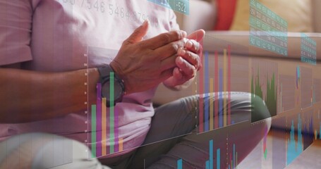Sitting senior Indian woman in pink at home, clasping hands on rug, smartwatch, floating charts