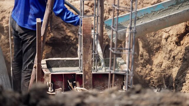 Concrete pump pours wet cement into a reinforced footing structure with steel bars, part of early stage building construction.