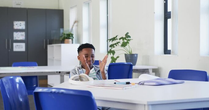 African American boy mid-clap, clapping then slowing and resting at classroom desk with headphones