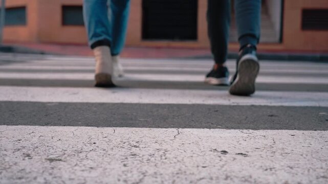 Low angle view of mother and young son legs cross city zebra crossing, boots and sneakers step together, conveying family bonding, safety and urban stroll