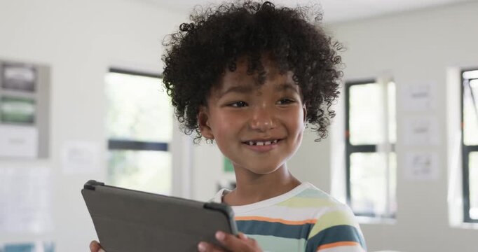 African American boy in striped shirt holding tablet case glancing down and studying in classroom