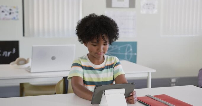 Tablet on white stand starting lesson, African American child at desk tapping and doing schoolwork