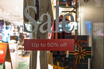 Window shop display advertising a large store sale of up to 50% off. Close up wide angle view, dressed mannequin and wrapped gift boxes, shallow depth of field, no people