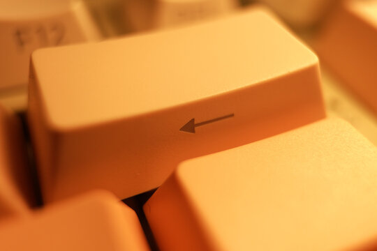 Macro close-up of a vintage mechanical keyboard backspace key with a left arrow symbol. Warm lighting emphasizes the retro plastic texture and nostalgic 90s computing technology.