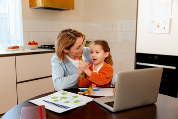 Mother juggling work and family, sharing laptop with daughter at home kitchen table