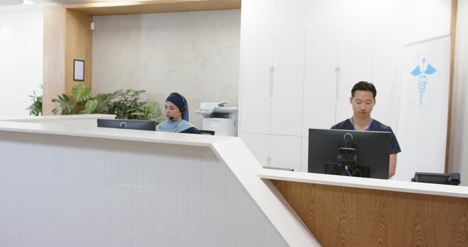 Diverse reception staff in scrubs responding to monitor prompts at clinic desk, typing for check-in