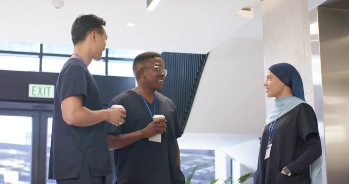 Diverse coworkers chatting during break after left Asian greeting, holding coffee with IDs in lobby