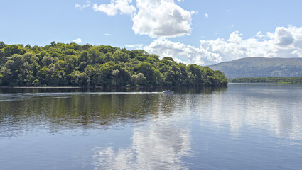 Fototapeta premium Man in a motor boat on Loch Lomond. Seen from the West Highland Way near Balmaha, Loch Lomond and the Trossachs National Park, Scotland.