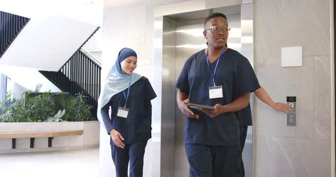 Diverse staff in navy scrubs pressing elevator button at lobby, tablet holder leading team exiting