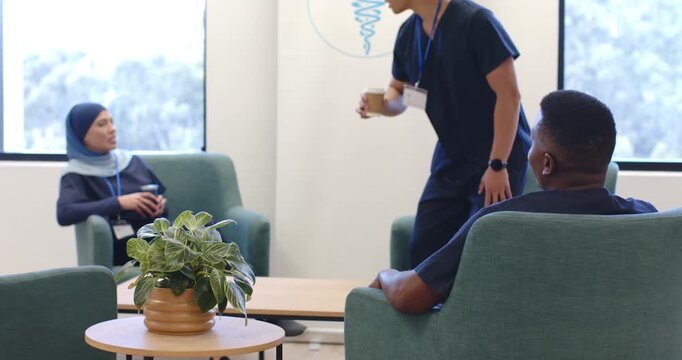 Diverse coworkers on break in staff lounge as Asian man holding coffee walking in, sitting, talking