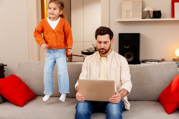 Father working from home with cheerful daughter jumping on sofa