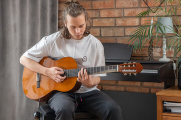 Young man playing classical acoustic guitar and practicing music at home. Teenager musician sitting...