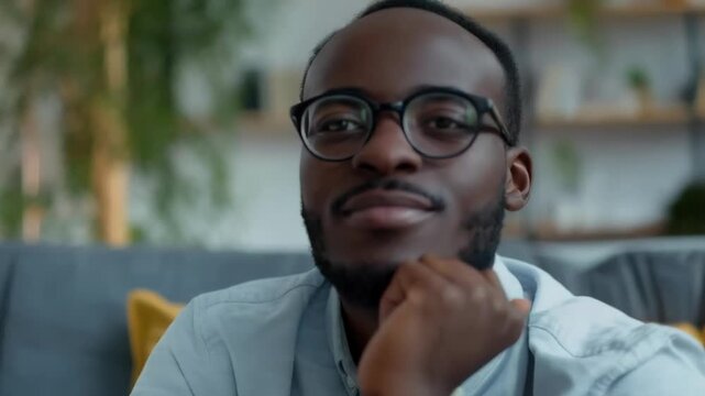 A smiling man wearing glasses and a shirt, sitting relaxed on a sofa, conveys a sense of comfort and confidence that is perfect for the background in materials about psychological well-being and remot